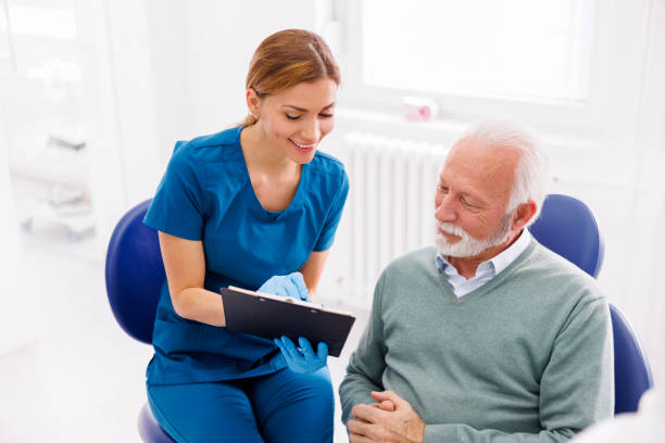 Senior man at doctor's office, health care specialist explaining medical procedure consent form to patient and taking patient's signature