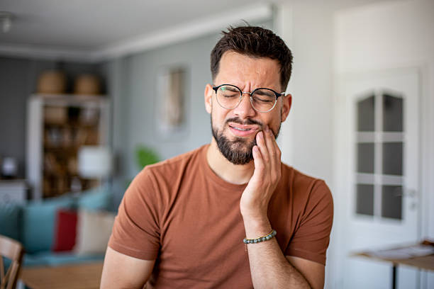 Young man suffering from a strong toothache, touching his cheek at home